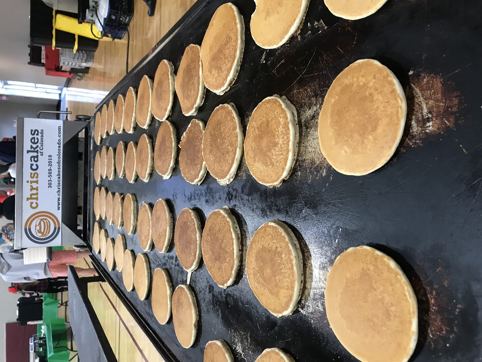 Full griddle of Chris Cakes of Colorado pancakes cooking at an indoor event